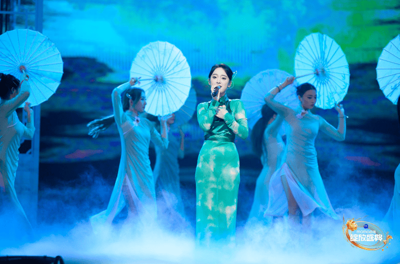 身着一袭墨绿色旗袍的她与舞台中的桃花,古门以及舞蹈演员们的油纸伞